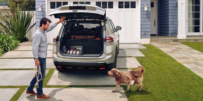 A man and his dog ready to jump into the spacious trunk of a 2024 Nissan Rogue in Pompano Beach, FL